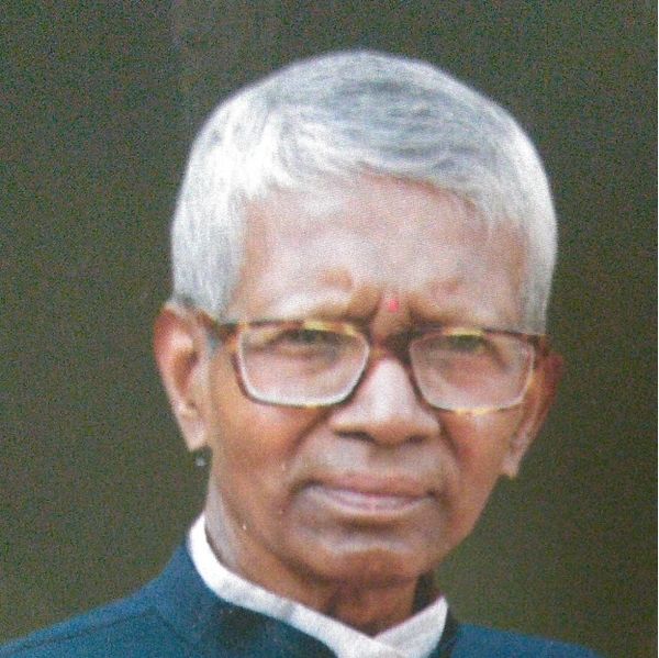 Elderly man with white hair and glasses, wearing a dark outfit.