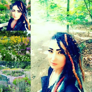 Woman with colorful braided hair in a garden and forest setting.