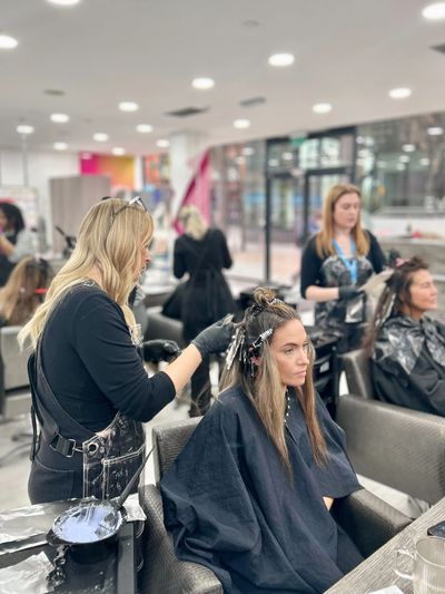 Blonde Evolve Academy student applying foils to hair. Other students working in the background.
