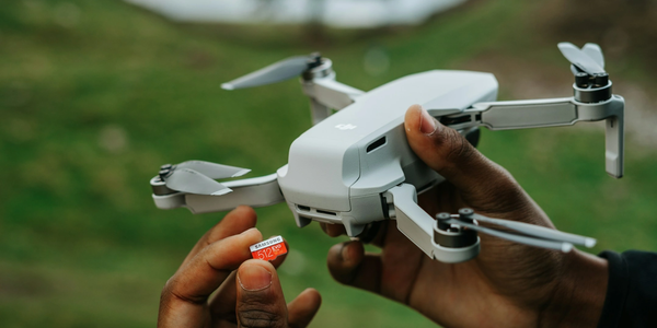 Person holding a drone and a 512GB microSD card outdoors.