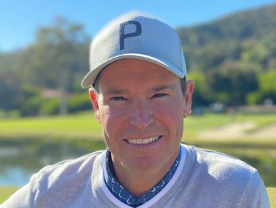 Smiling man wearing a gray cap outdoors on a sunny day.