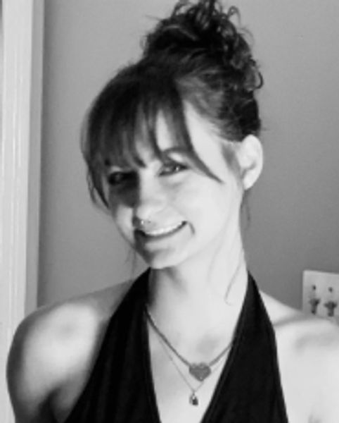 Black and white portrait of a smiling woman with a high bun and layered necklaces.