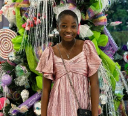 Smiling girl in pink dress standing in front of a decorated Christmas tree. fundraiser, community support, childhood illness, 501(c)(3) nonprofit, houston county, warner robins, kethleen, perry, lake joy