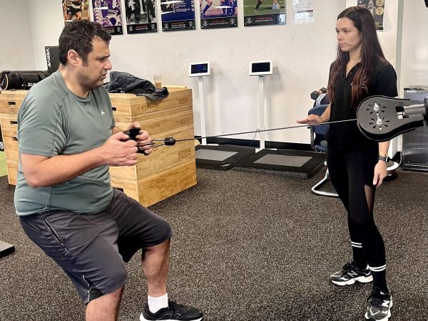 Man exercises with resistance band while woman supervises in gym.