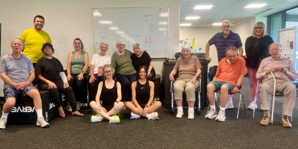 Group of seniors and trainers posing in a fitness room.