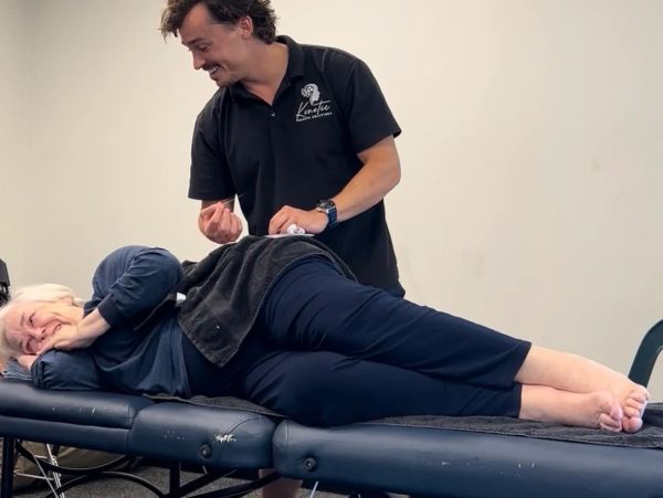 A therapist treats a patient lying on a massage table in a clinical setting.