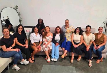 Group of ten women sitting and smiling indoors.