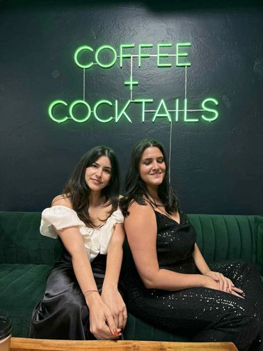 Two women sitting under a green neon sign.