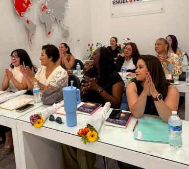 Women sitting and clapping in a classroom setting.