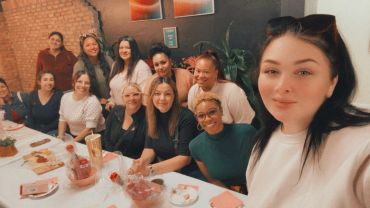 A group of women smiling for a selfie at a table.