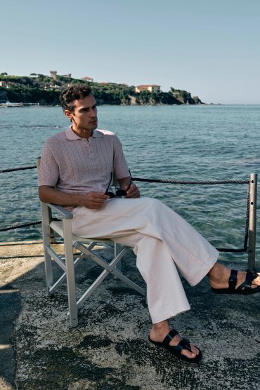 Man in light outfit sitting by the seaside on a chair.