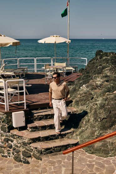 Man in striped shirt walking down stone steps by the seaside.
