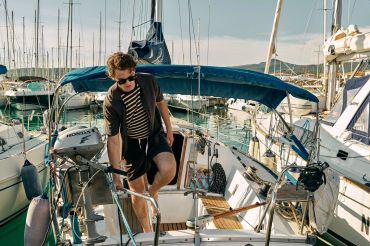 A man prepares a sailboat at a marina on a sunny day.