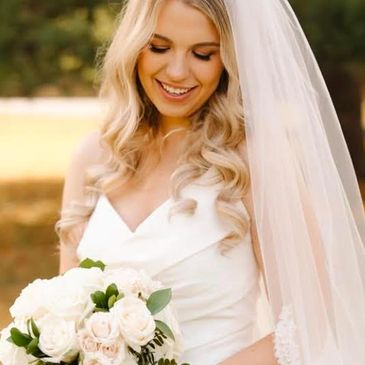 Smiling bride in white gown holding a bouquet of white and blush roses.