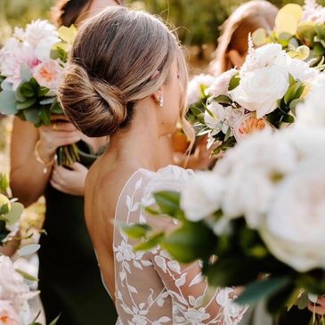 Bride with elegant updo and lace dress surrounded by floral bouquets.