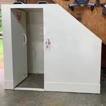 Custom white storage cabinet with angled top and open door in workshop.