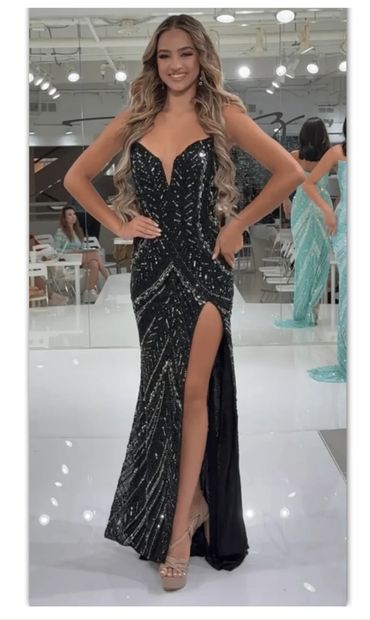 Woman in a sparkling black evening gown with a thigh-high slit and long wavy hair.