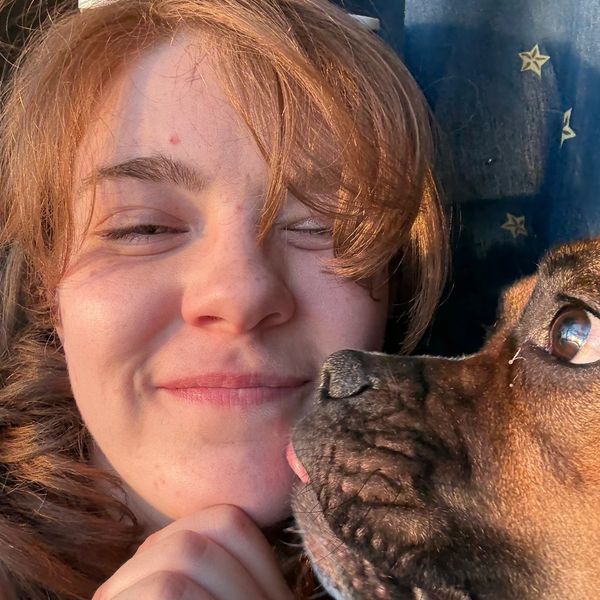A woman smiles as a dog affectionately licks her face.