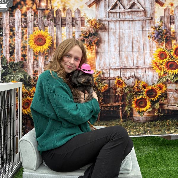 Girl hugging a small dog wearing a pink hat with sunflower backdrop.