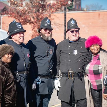 Group photo with three policemen in vintage uniforms and two women outdoors.