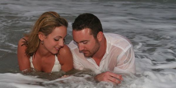 Couple lying in ocean water, smiling and relaxed.