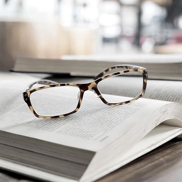 A pair of eyeglasses sitting on an open book with a window in background