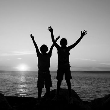 Two people standing with their arms in the air at a beach with a sunset in background