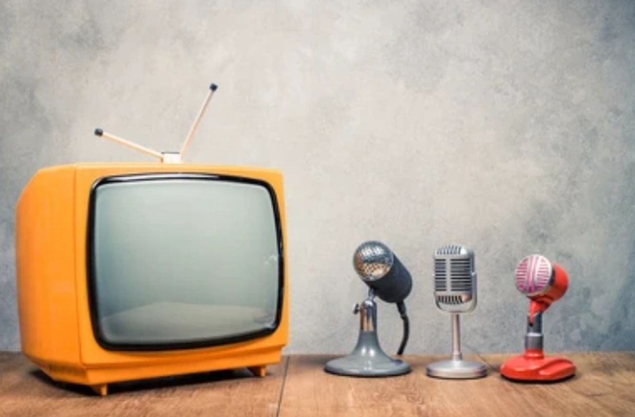 Retro orange TV with three vintage microphones on wooden table.