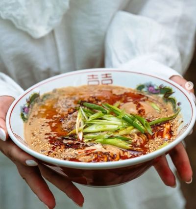 A bowl of spicy ramen topped with green onions held by a person.