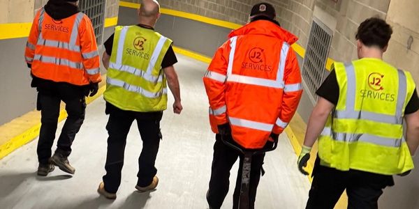 Four workers wearing J2 Services safety vests walk down a corridor.