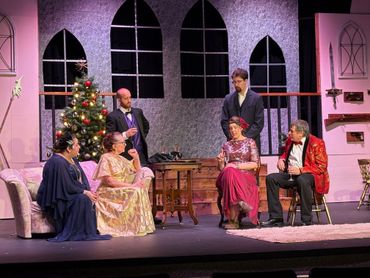 Actors in formal and festive attire on a stage set with a Christmas tree and medieval decor.