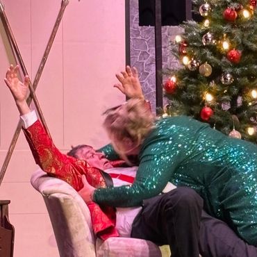 Actors perform a dramatic scene near a decorated Christmas tree on stage.