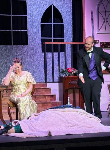 Actors performing a dramatic scene on stage with a covered body and expressive gestures.