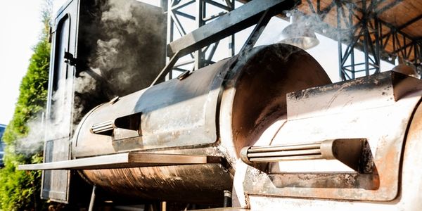 three wood fired smokers with smoke rolling out of them