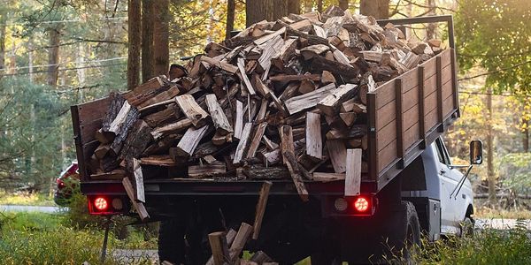 a truck loaded with firewood raising the bed, preparing to dump out the wood onto the ground