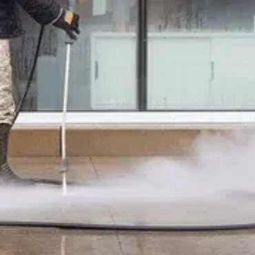 Person cleaning floor with a high-pressure washer producing steam.