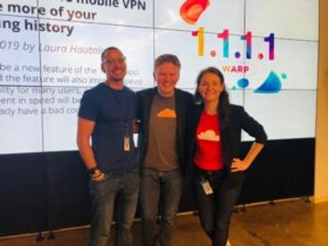 Three people smiling in front of a 1.1.1.1 Warp display screen.