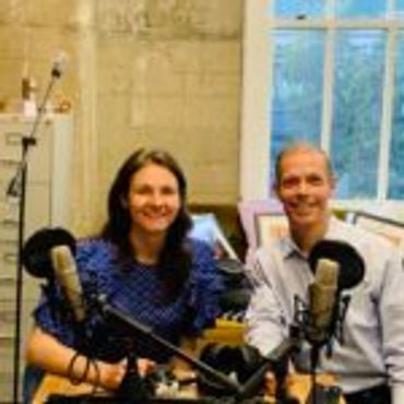 Two people smiling with microphones in front of them indoors.