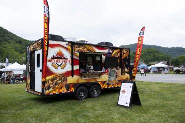 Food truck serving Philly cheesesteak at an outdoor festival with mountain backdrop.