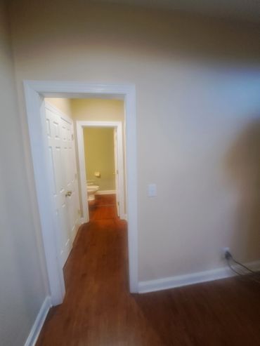 Hallway leading to a bathroom with wooden floors and white doors.
