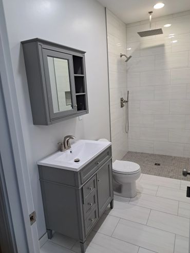 Modern bathroom with gray vanity, mirror cabinet, and walk-in shower.
