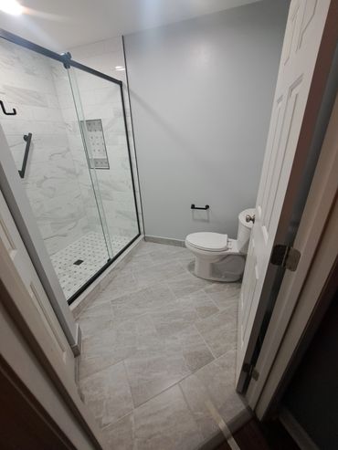 Modern bathroom with glass shower and light gray tiles.