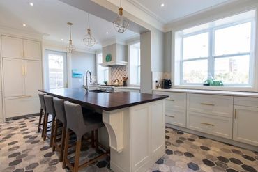White kitchen cabinets with gold hardware. Dark brown wood top island with sink. Hexagonal tiled flo
