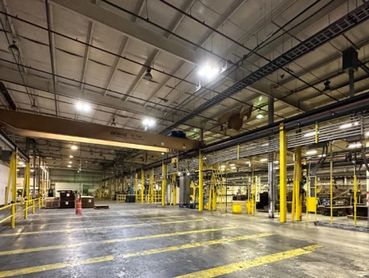 Empty industrial warehouse with yellow safety markings and overhead crane.