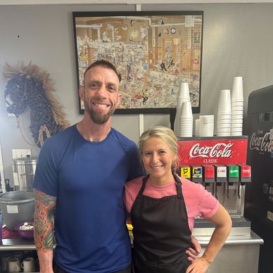 Two people smiling in a casual setting near a soda dispenser.