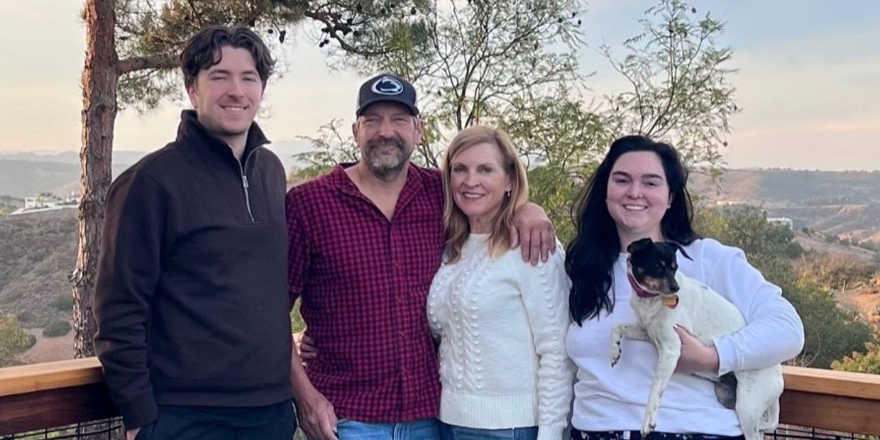 Four people and a dog posing outdoors with scenic hills in the background.