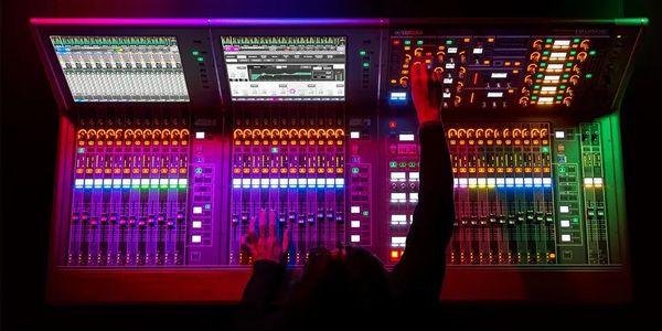 Person operating a brightly lit sound mixing console in a dark room.