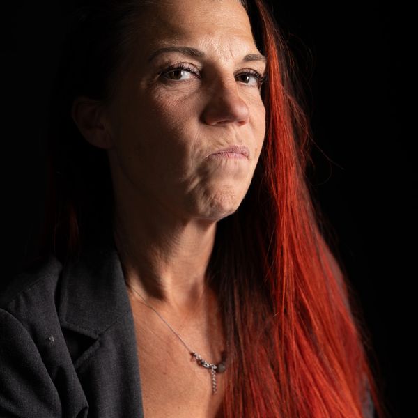 Woman with long red hair and serious expression against black background.