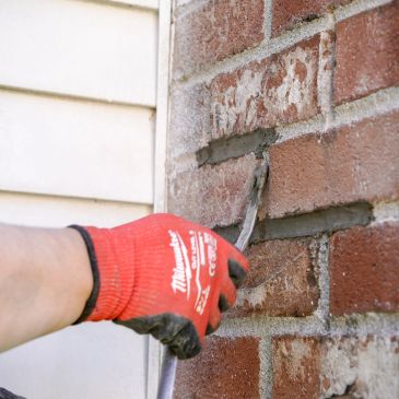 Person wearing red glove repairing brick mortar with a trowel.
