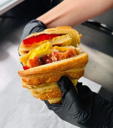 Hand holding a croissant sandwich with eggs, bacon, and red pepper.